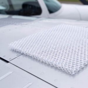 Close-up of a white mesh fabric laid over the hood of a silver car, with a side mirror in the background.